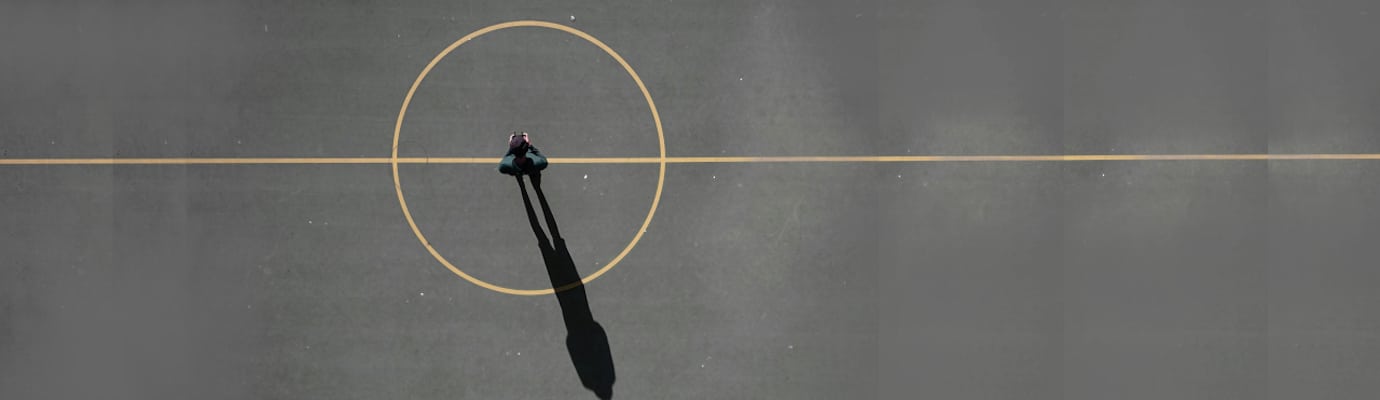 Mensch steht auf grauem Grund in der Mitte einer runden Spielfeldmarkierung. Er wirft einen langen Schatten.