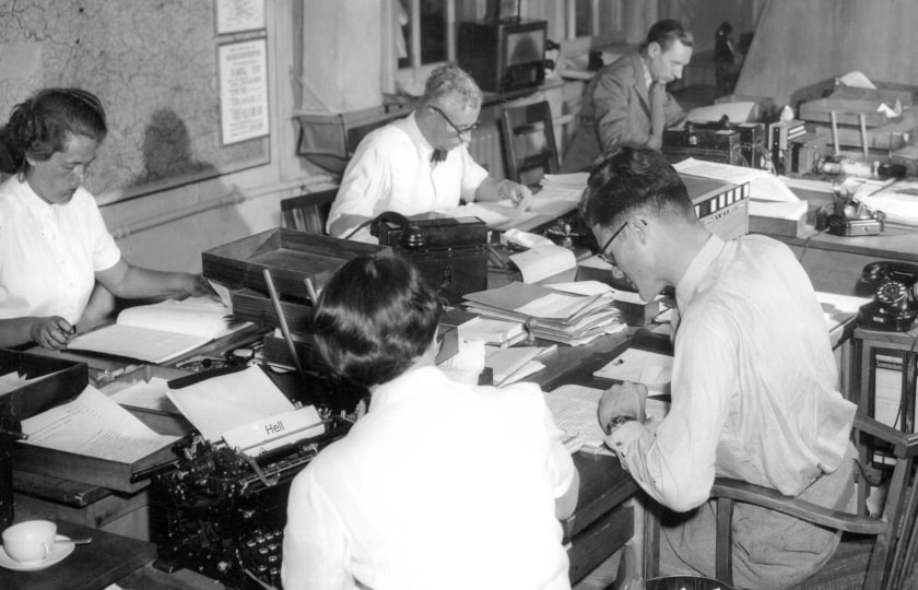 Blick in die dpa-Redaktion von 1956, mehre Menschen sitzen schreibend an einem großen Tisch