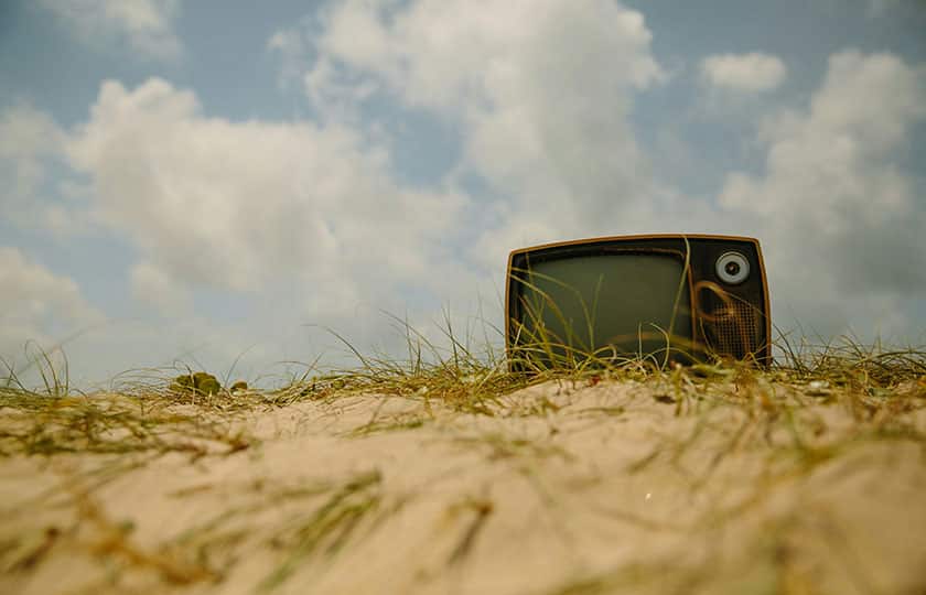 ein altmodischern Fernsehen liegt auf einer Düne vor blau-weißem Himmel