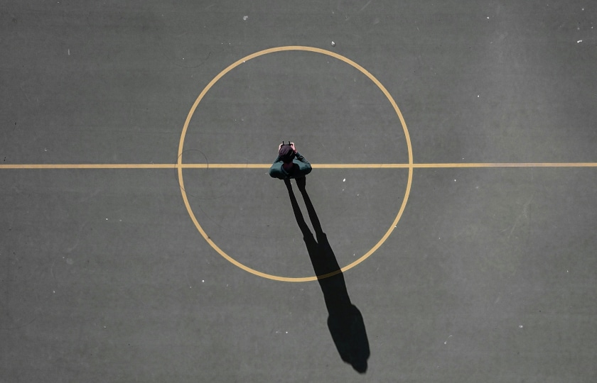 Mensch steht auf grauem Grund in der Mitte einer runden Spielfeldmarkierung. Er wirft einen langen Schatten.