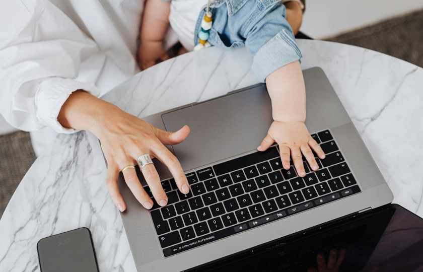 Hand eines Erwachsenen und eine Babyhand tippen auf Laptoptastatur