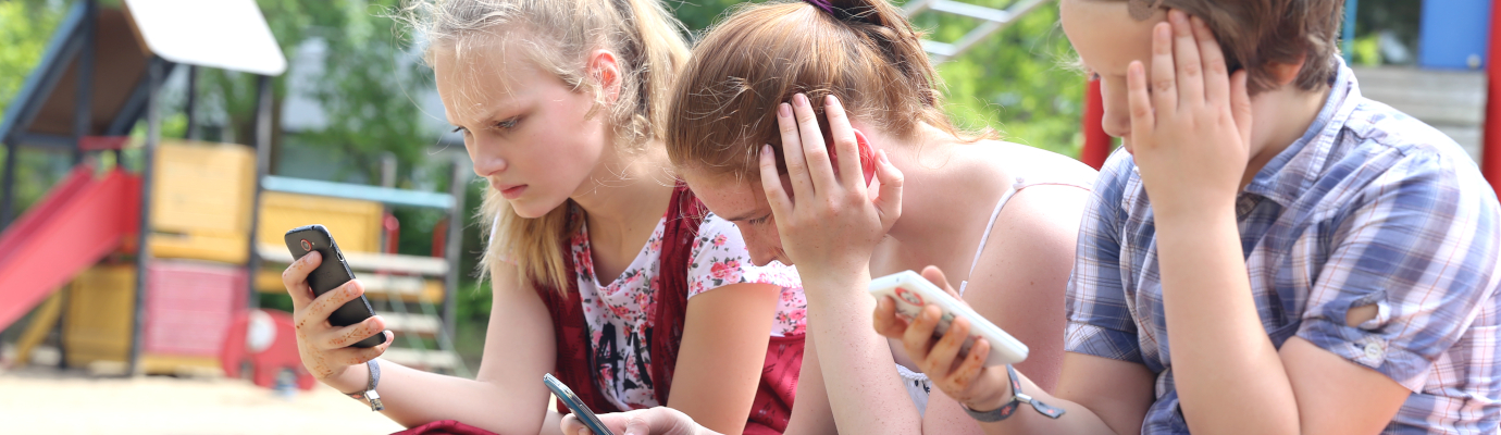 Drei Kinder starren in ihre Smartphones.