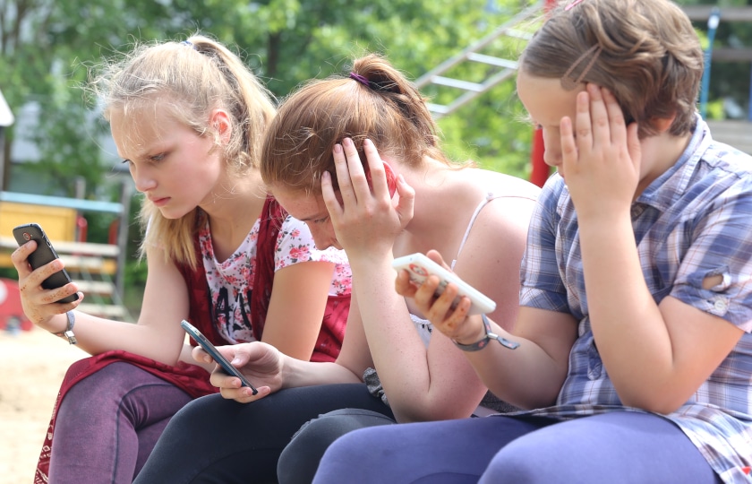 Three girls on a playground staring at their smartphones