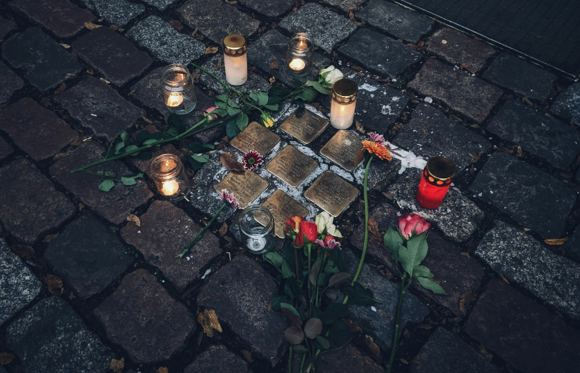 Stolpersteine mit leuchtenden Kerzen und Rosen drum herum.