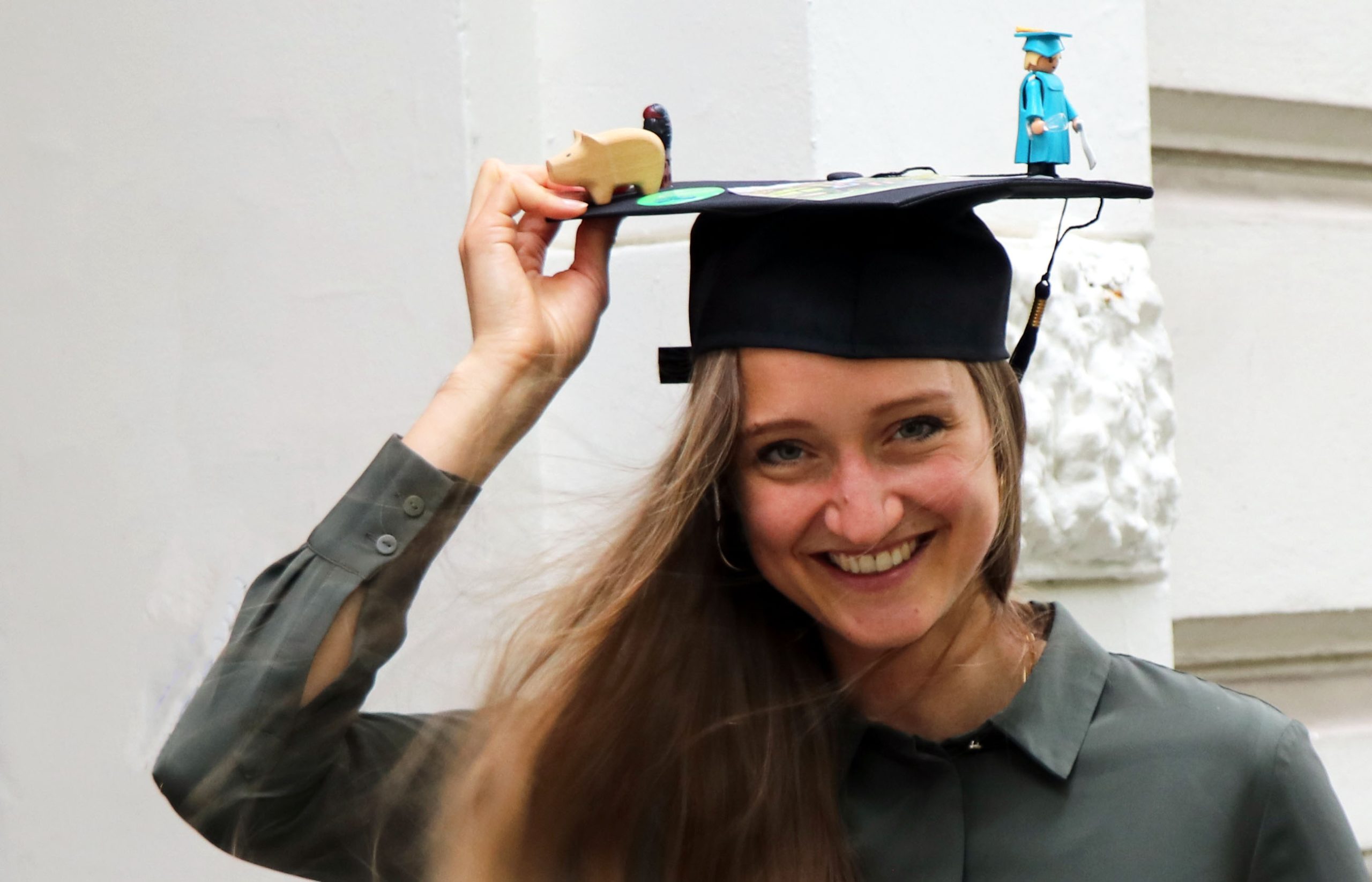 Leonie Wunderlich hält ihren Doktorhut fest, der davonzufliegen droht