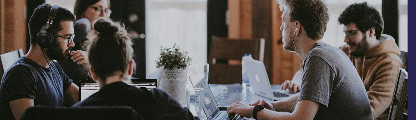 Fünf junge Erwachsene, einige mit Laptop und Kopfhörer, sitzen um einen Tisch und diskutieren.