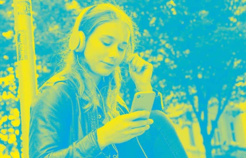 Ein Mädchen sitzt mit Kopfhörern und schaut in ein Handy