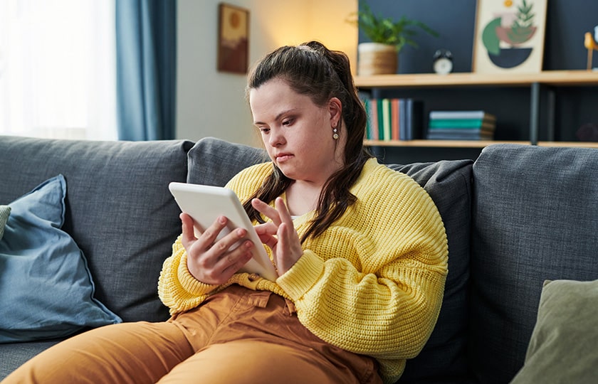 Mädchen mit Down Syndrom sitzt auf der Counch surft mit ihrem Tablet im Internet