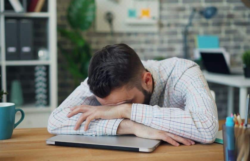 Ein Mensch stützt seinen Kopf an einem Tisch auf seinen Laptop für eine Pause.