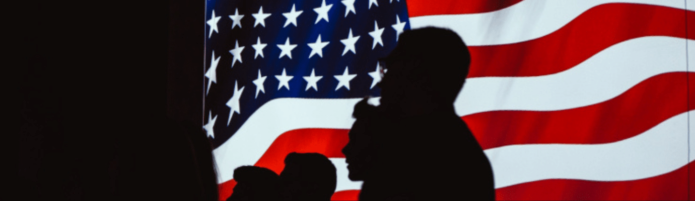 Silhouettes of three people in front of a large American flag