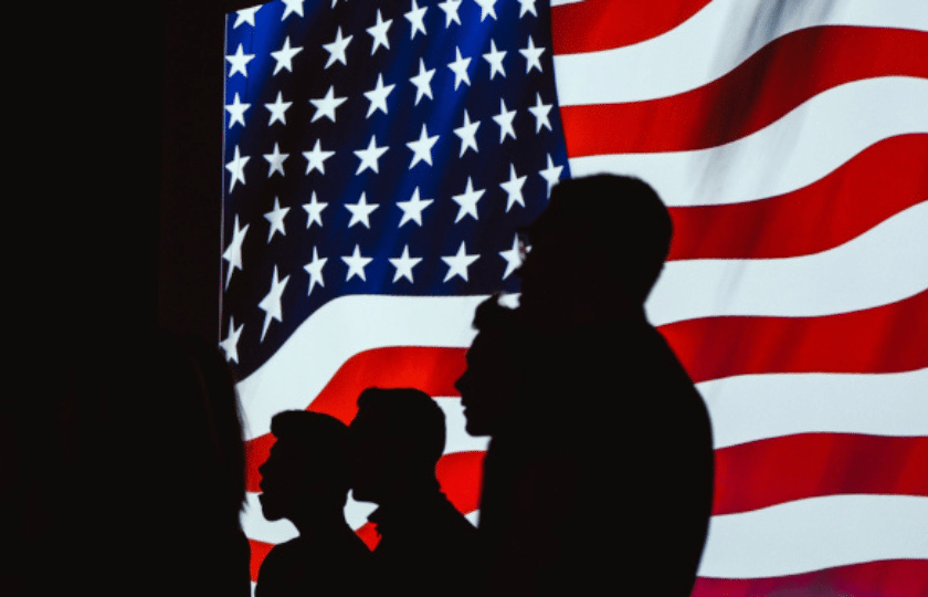 Silhouettes of three people in front of a large American flag