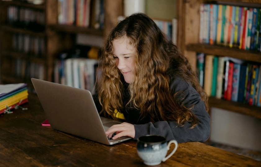 Ein Mädchen schaut gebannt in einen Laptop. Hinter ihr ist ein Bücherregal.