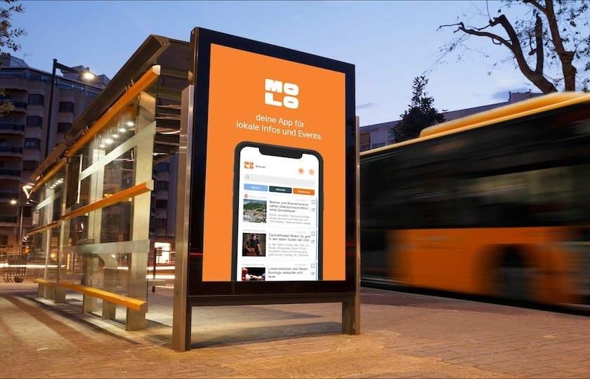oranges Reklameschild, das für die App Molo wirbt, an einer Bushaltestelle